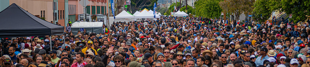 Crowd filling a San Francisco street, with tents, trees, and buildings in the background.