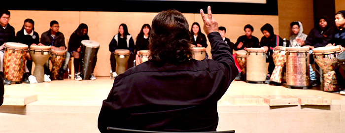 Man making a peace sign in front of a youth drumming group